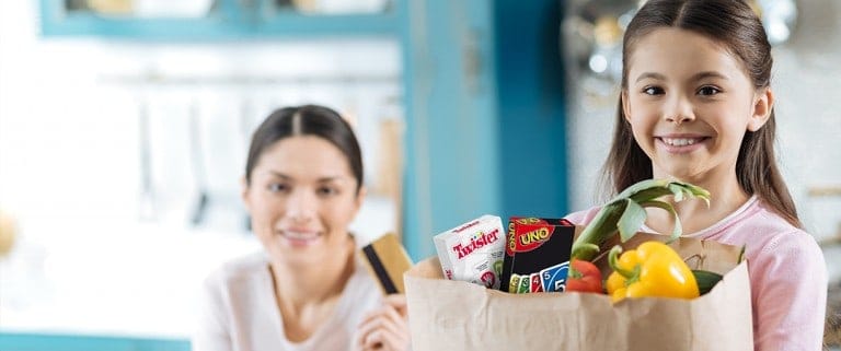 Frau mit Kind, welches Einkaufstüte in der Hand hält und Pocket Game Twister sowie Uno schauen heraus.